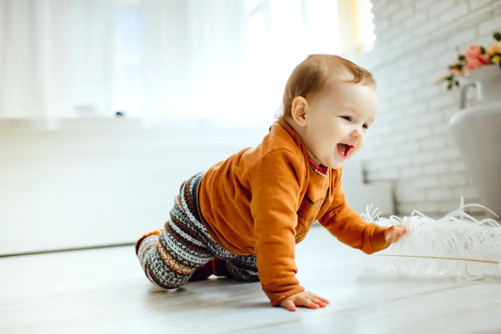 Happy child in an orange sweater playing with a feather on the floor