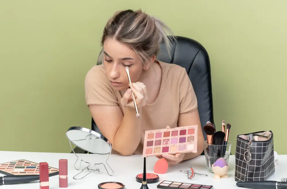 Young woman applying makeup at a desk mirror