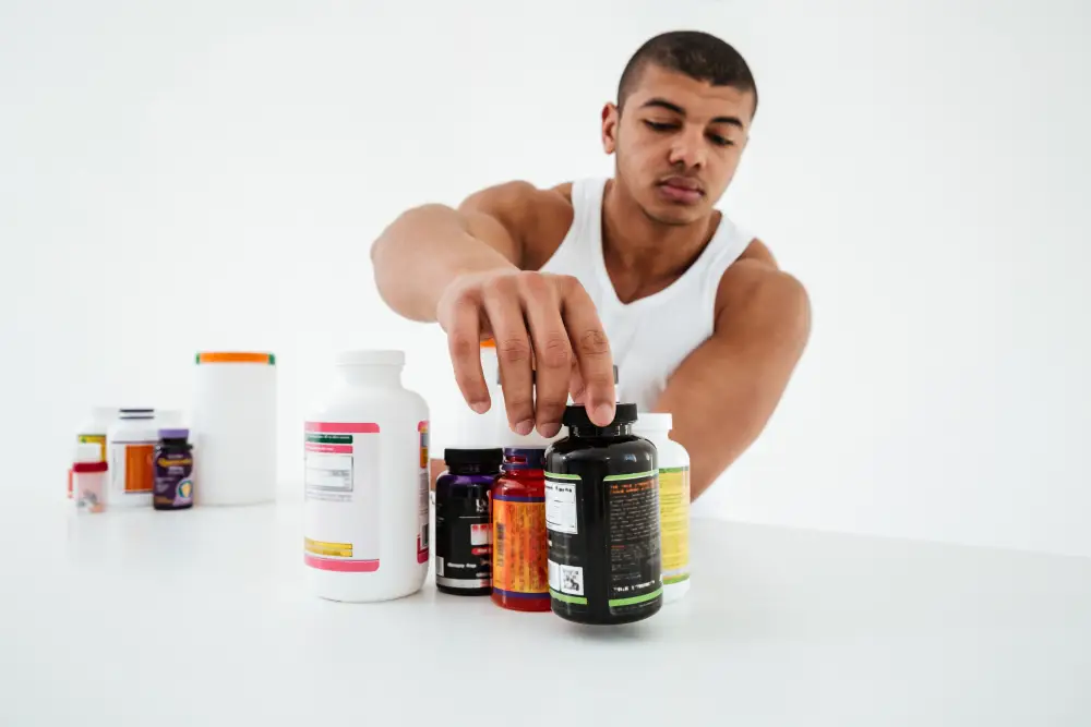 Sportsman standing against a white wall holding vitamins